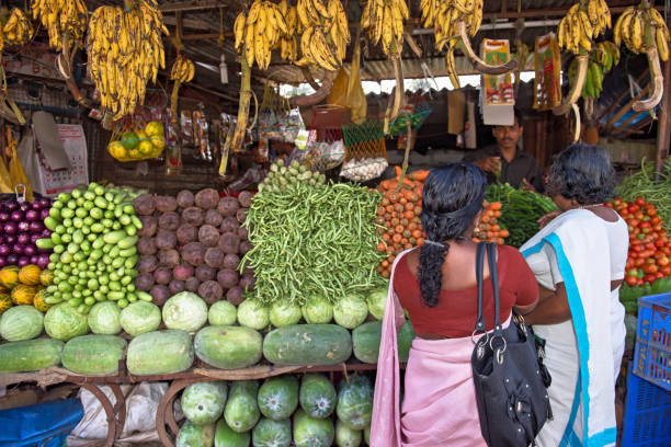 Cherthala,Kerala,India - January 15, 2013: Two Indian ladies standing in front of a  market stall with vegetables and fruits in Cherthala, a location in the Alappuzho district of Kerala, about 30 km south of Kochi.